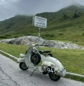 Faro Basso stehen vor dem Passchild des Flexenpass - im Hintergrund Berge und tiefe Wolken