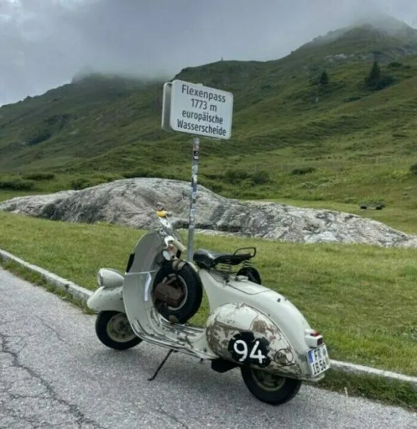 Faro Basso stehen vor dem Passchild des Flexenpass - im Hintergrund Berge und tiefe Wolken