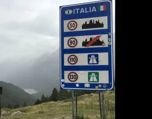 Schild mit Angaben von Tempolimit Italien mit Blick in ein Tal und See