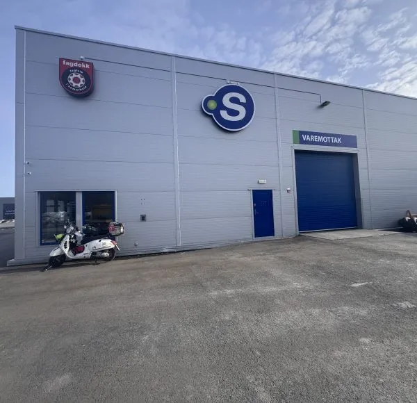 Weisse Vespa GTS steht vor einer grauen Werkstatt-Halle mit den Logos von 