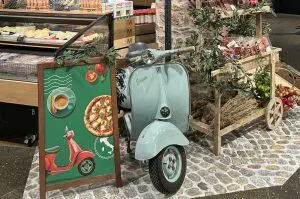 Vespa VNB125 steht zwischen Ständen mit Salami und Käse im Migros Winterthur 11-2024